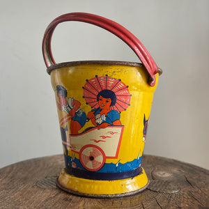 A Vintage Child's Tin Beach Bucket in sunny bright colours. The delightful scene on the side shows a donkey pulling along a lad giving a lift to a young lady with her parasol. These tin buckets are becoming increasingly rare and are very collectable - SHOP NOW - www.intovintage.co.uk