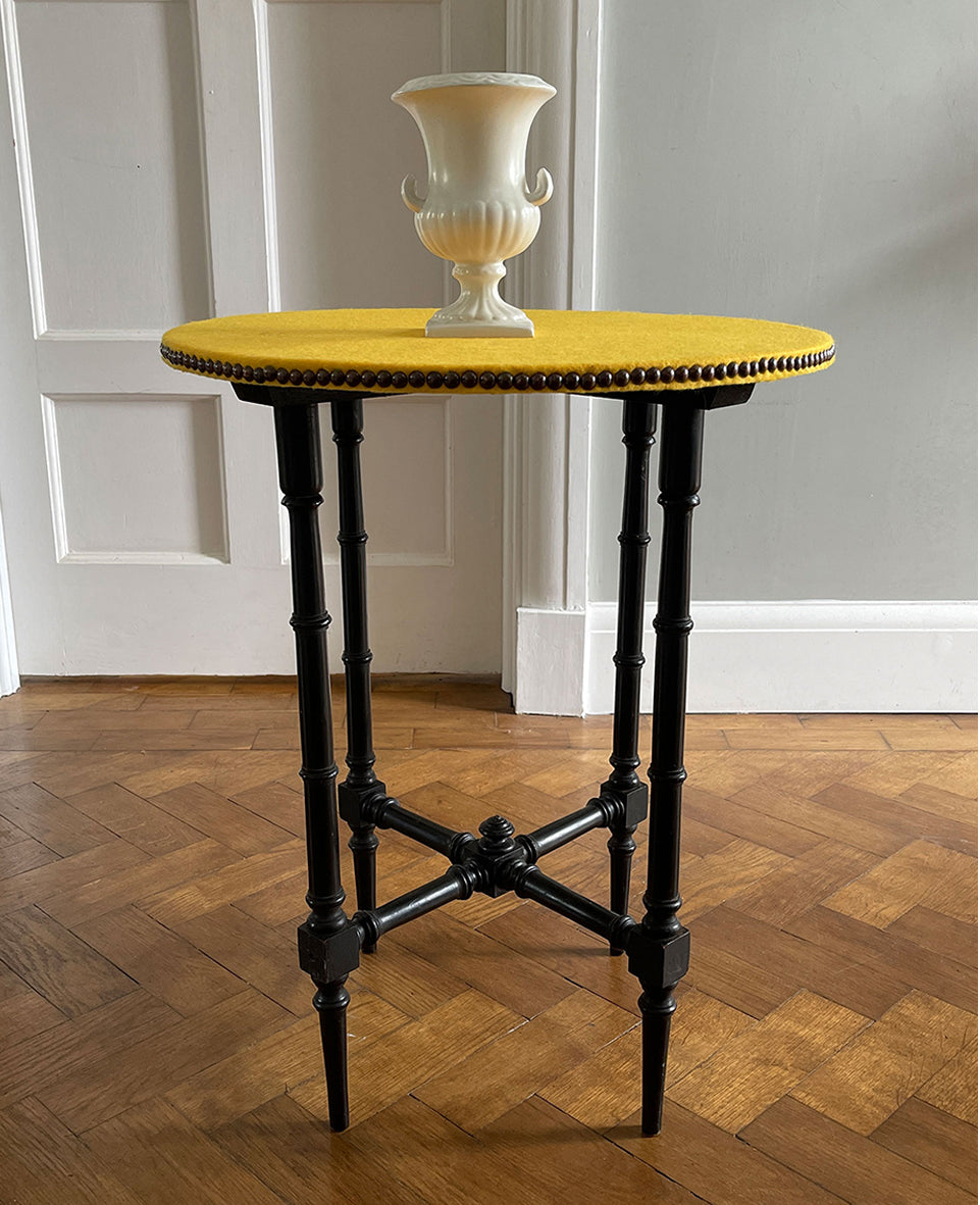 A pretty Victorian table in the Aesthetic manner in its original ebonised finish. The top sees a re-finished yellow felt top with brass studding to the edge, whilst underneath sees four turned ebonised legs and crossed turned stretchers and central turned boss. - SHOP NOW - www.intovintage.co.uk